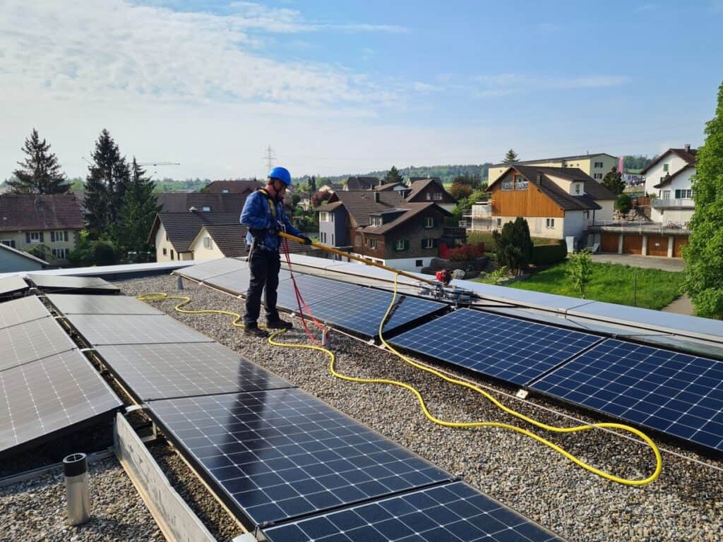Outclean-Techniker bei der fachgerechten Reinigung von Solarmodulen auf einem Einfamilienhaus in Basel mit Osmosewasser und Sicherheitsausrüstung.